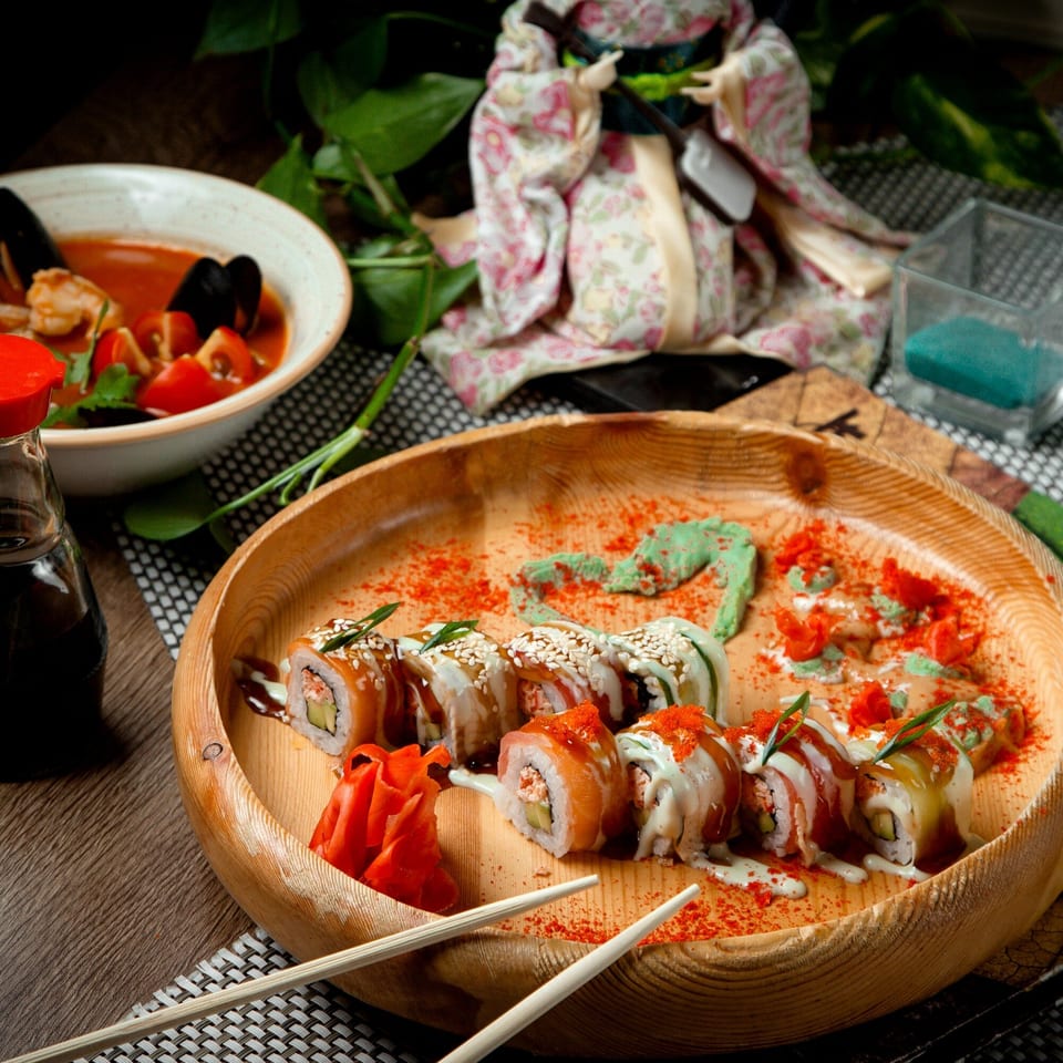 Assorted sushi rolls with ginger, wasabi, and soy sauce, alongside a bowl of seafood soup.